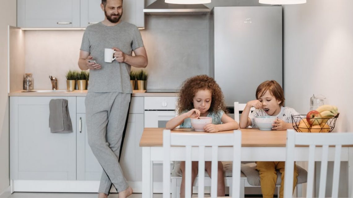 A father with two children enjoying breakfast in a bright, modern kitchen at home.